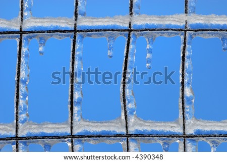 Close-up of ice built up on a wire fence in winter, against blue sky