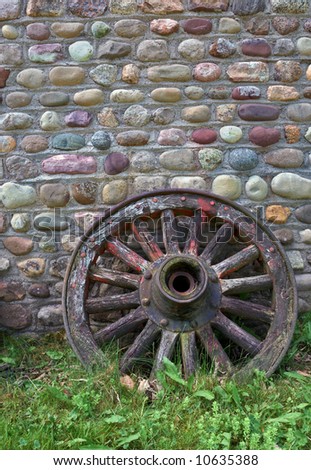 Antique wagon wheel against cobblestone wall