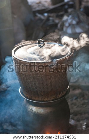 black pot boiling water for cooking rice on the fired stove next to firewood pile, Thailand north east local method