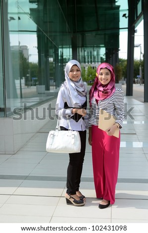 Two young pretty Asian muslim business woman in head scarf shake hand together