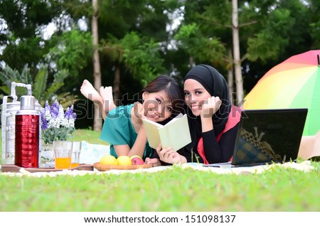 Portrait of pretty young Muslim woman sharing idea with laptop and reading book