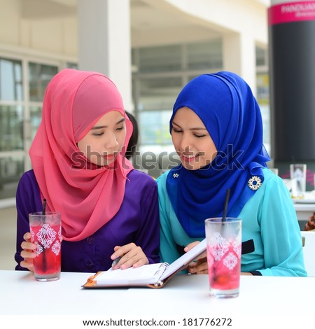 Young asian muslim woman in head scarf  exchanging ideas and taking notes
