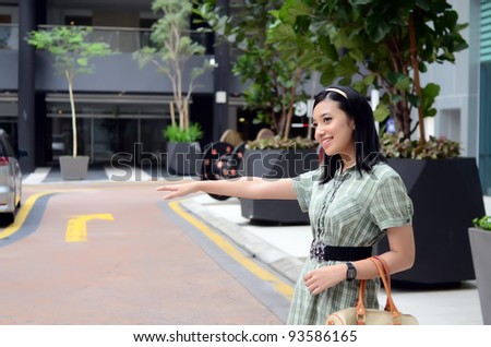 Lovely of young Asian businesswoman hailing a taxi cab outside a office