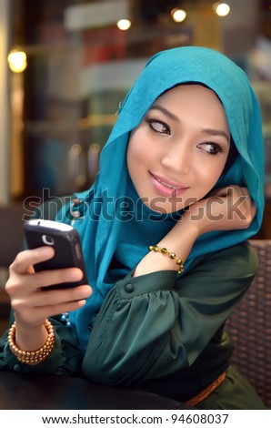 Portrait of beautiful young Asian Muslim business woman texting on her phone outdoor