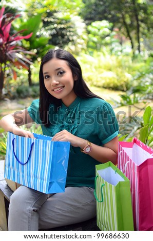 Lovely attractive and smiling young Asian woman with shopping bags at garden