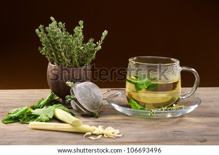 Tea strainer, and a cup of grass on a wooden table.