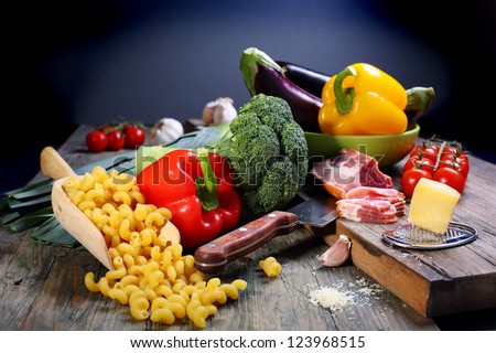 Vegetables, pasta, bacon and table knife on a wooden table.