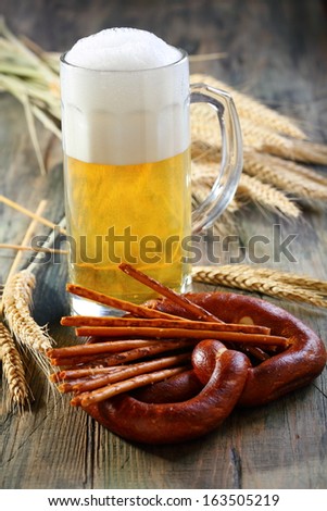 Pretzel, salty sticks and glass of beer on a wooden table.