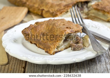 Piece of meat pie with fork and knife on a white plate.