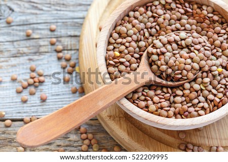 Lentils and spoon in a wooden bowl close up on an old table.