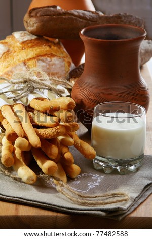 Italian bread sticks in a paper bag, a glass of milk and a ceramic jug.