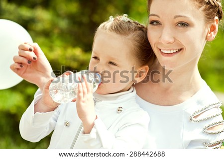 Beautiful little girl is drinking water on the hands of her mother in a park a sunny summer day.