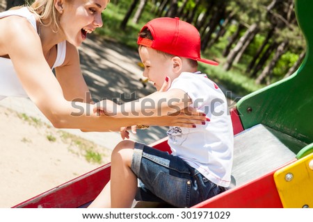 Mother and son playing together outdoors in park laughing ride on the swing