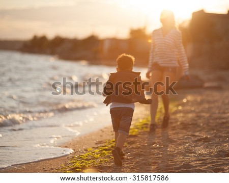 Beautiful boy with a woman relaxing on the beach. Throw pebbles into the sea, running, jumping, laughing and having a great time with each other at sunset.