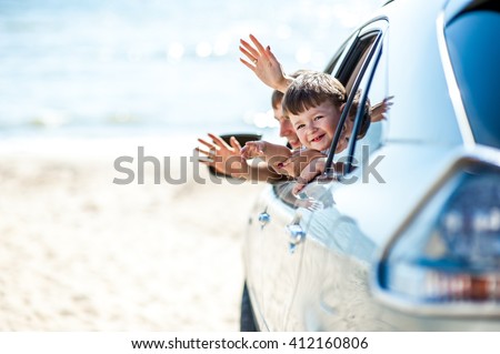 Portrait happy, smiling kid sitting in the white, silver car looking out windows, ready for vacation trip, outdoor background. Positive Human face expression, emotions, feelings