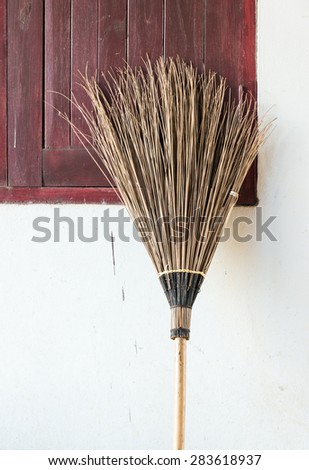 Old coconut brooms is laying near the window of countryside house.