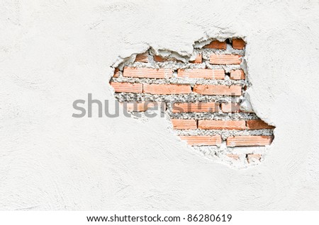 White wall which cracked until see the orange brick inside.