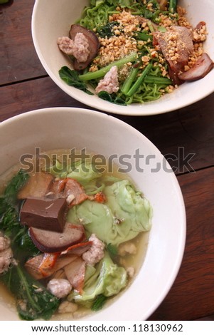 Closeup of asian stir fry with handmade green noodle, pork, vegetables, bean sprouts, and sesame seeds in a white bowl on wooden table.
