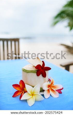 Coconut, beach cafe, plumeria on blue table with blurry beach background