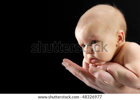Newborn baby safe in the hands of his father. Black background. Copy-space on the left.