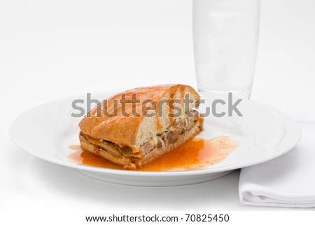 Mexican Torta Ahogada, or drowned sandwich with pork on a white plate with glass of water.