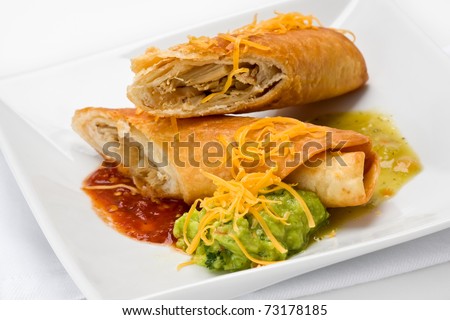 Flautas with green and red sauce topped with cheese on a white plate.