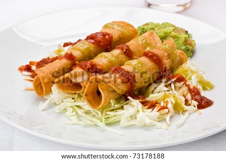 Three taquitoes on a bed of sliced cabbage with guacamole, red and green salsa, on a white plate.