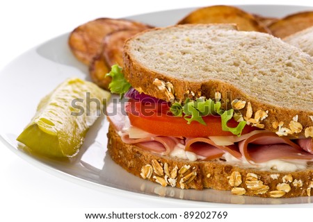 Ham sandwich with swiss cheese, lettuce and tomato with homemade potato chips on a white plate.