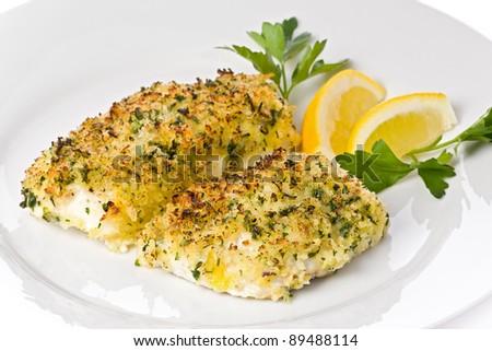 Baked cod with breadcrumbs on a white plate garnished with lemon slices and parsley.