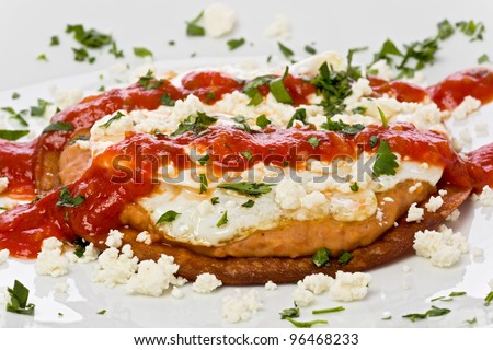 Fried corn tortilla with refried beans, fried egg, crumbly cheese, and topped with a spicy chili sauce.