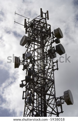 Silhouetted mobile cell phone transmitter aerial. This mast is covered in dishes and antenna.