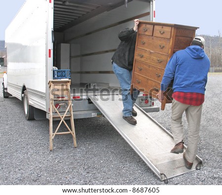Two men carry chest of drawers onto a moving van
