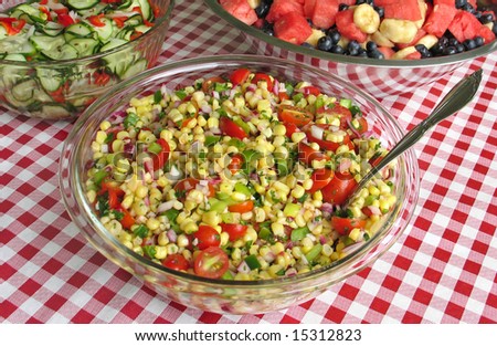 Fresh corn salad, accompanied by cucumber and fruit salads on a picnic buffet