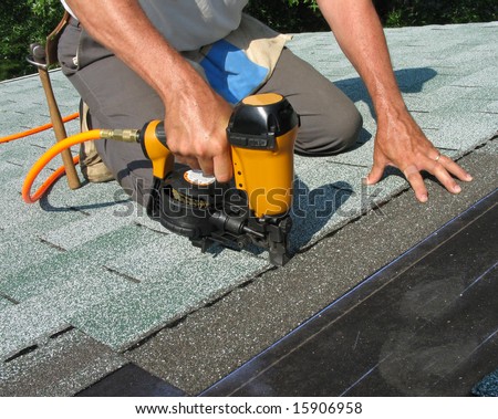 Carpenter uses nail gun to attach asphalt shingles to roof