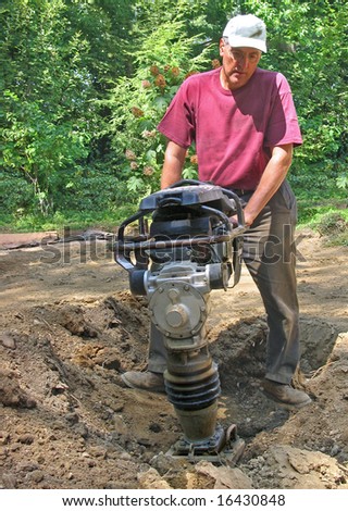 stock photo : Man uses compactor to firm soil at worksite