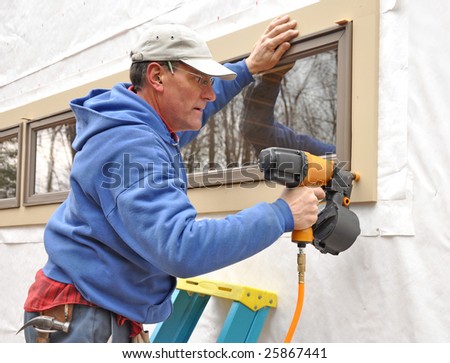 Carpenter using nail gun to install trim around windows