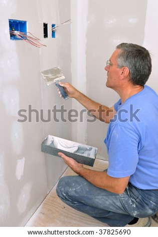 Man using drywall knife to finish seam between drywall sheets