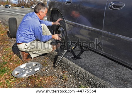 Man changing flat tire along a busy highway