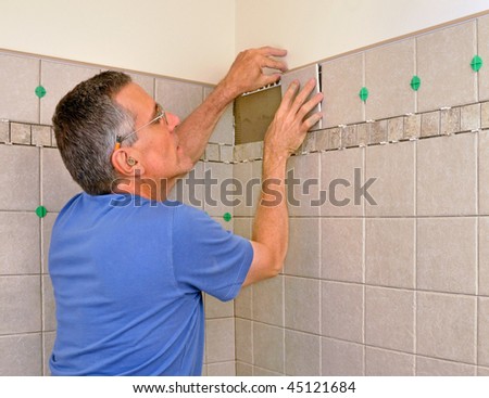 Man installing ceramic tiles on bathroom wall in shower area