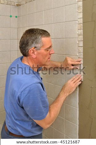 Man installing border of small ceramic tiles on bathroom wall in shower area