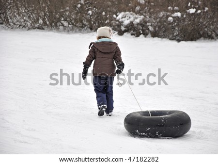 Young girl pulling inner tube up sledding hill