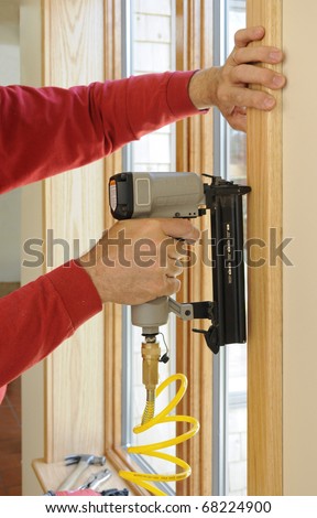 Nail gun being used to install wood trim around windows with finishing nails