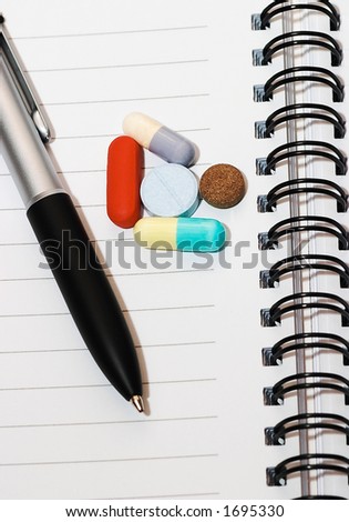 Empty blank ring, notepad, one black pen on white page with pills to indicate relation with pharmaceutical industry, or metaphor for office/school stress or work-related drug research