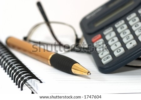 Note pad with pen, calculator, and glasses. glasss on table depicts tiredness