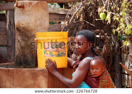 August 2014-Franciscan Mission of Pomerini-Tanzania-Africa-A mother with her ??child while it fills a bucket of drinking water to the public fountain of the Franciscan Mission of Pomerini.