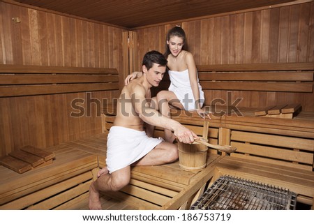 Young couple in sauna. Handsome man pouring water on hot rocks in sauna