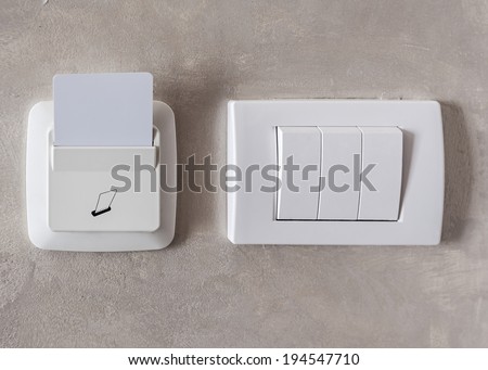 Electronic lock with card inserted and light switches on concrete wall in hotel room