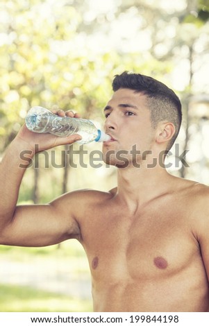 Young muscular man with no shirt drinking water in the park