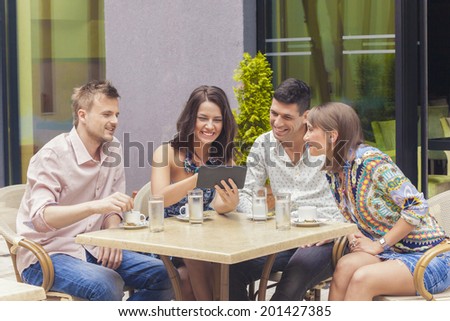 Two couples drinking coffee, smiling, chatting and watching video on tablet pc in cafe bar
