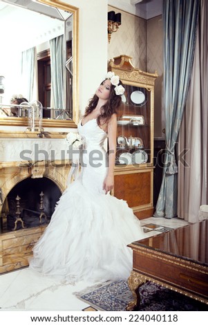 Beautiful bride with elegant white wedding dress posing in front of marble fireplace